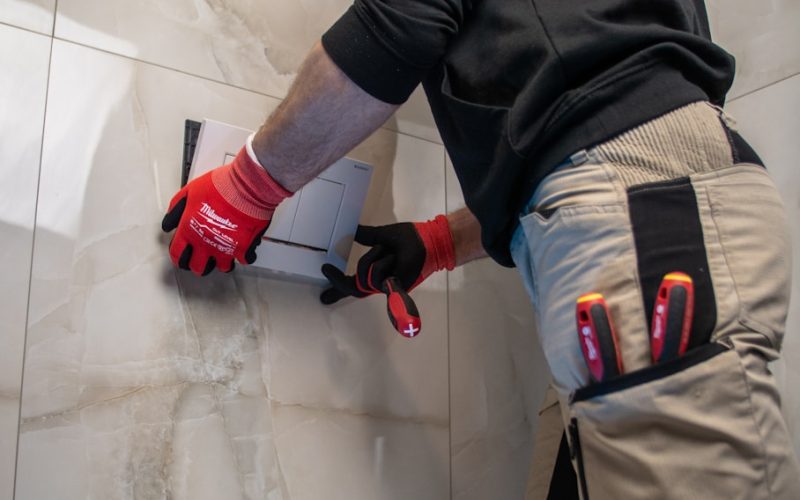 a man in a black shirt and red gloves working on a toilet